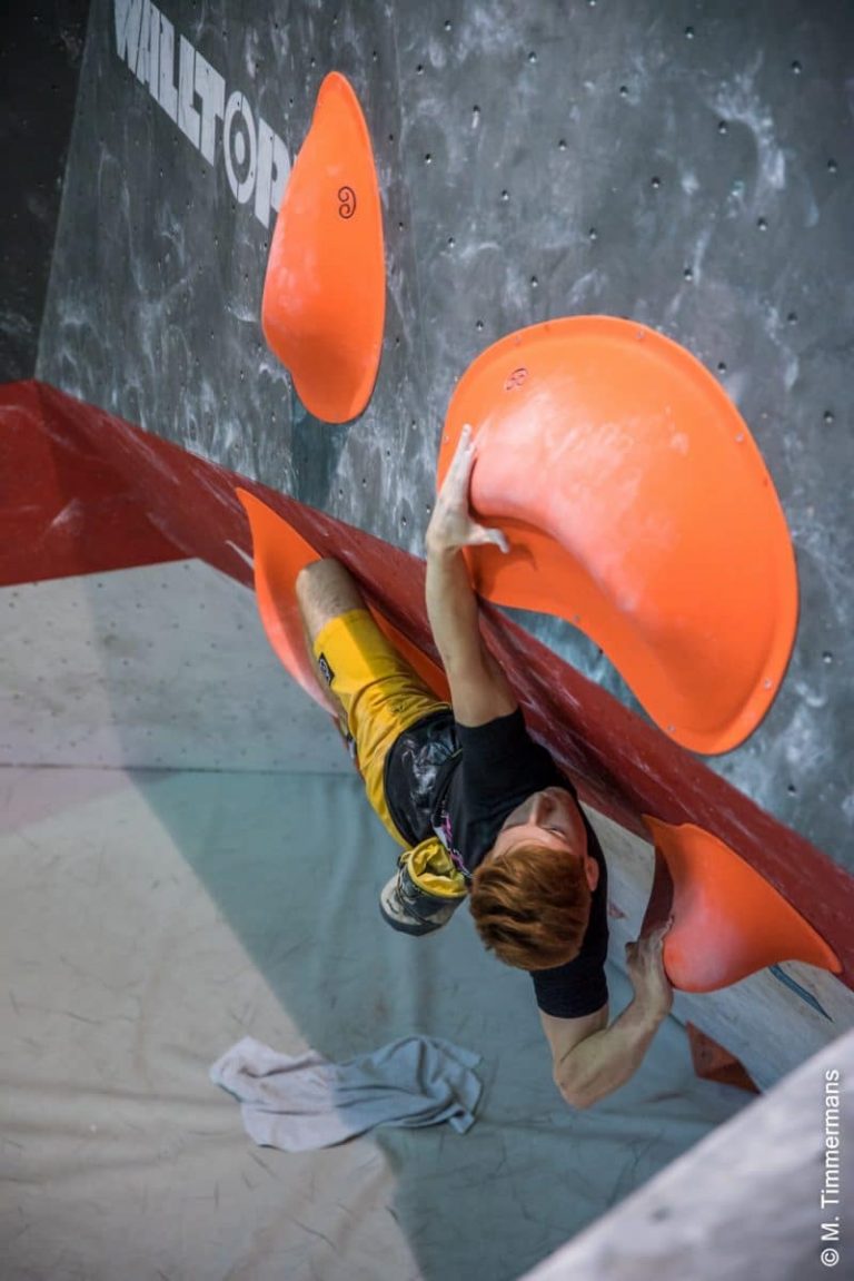 The Art of Route Setting 4 Climber reaching for an orange macro on a steep competition wall
