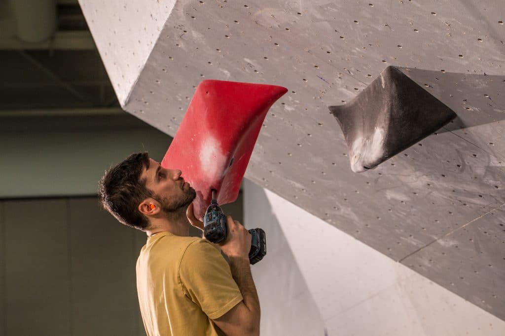 The Art of Route Setting 2 Route setter fixing a red macro on a competition wall